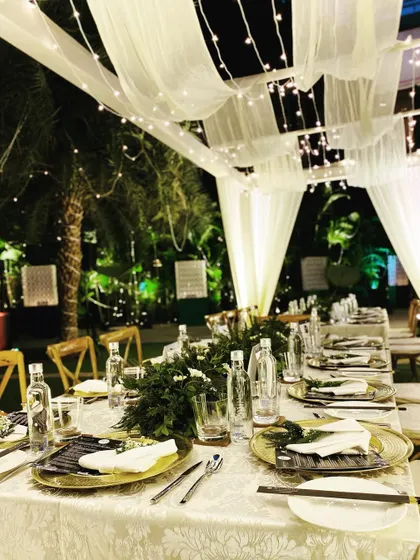 A detailed look at the tablescape for the intimate courtyard dinner. The combination of lush greenery, metallic charger plates, and classic tableware creates a look of understated elegance.