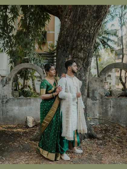 Showcasing classic Marathi elegance, this couple's portrait is set against a rustic tree and stone wall. Her deep green Nauvari saree and his white kurta create a timeless look, perfect for heritage-themed engagement photos.