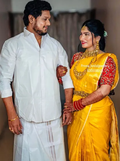 The couple in their traditional wedding attire. The bride's yellow saree and temple jewellery perfectly match the groom's simple and elegant white outfit.