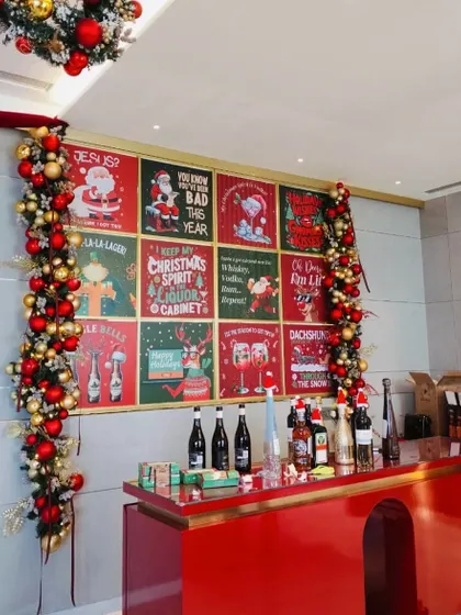 A festive bar setup with a custom backdrop of vintage-style Christmas posters and garlands of red and gold ornaments.