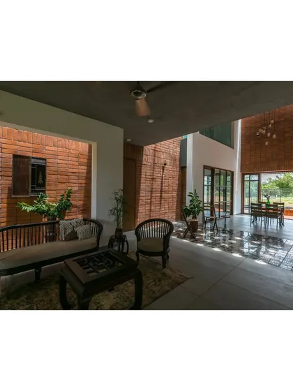 The semi-open living area in 'An Earthy Affair' is designed to feel like a veranda, protected from the elements but visually connected to the garden. The dappled light filtering through the trees and the use of natural materials create a tranquil space for relaxation.