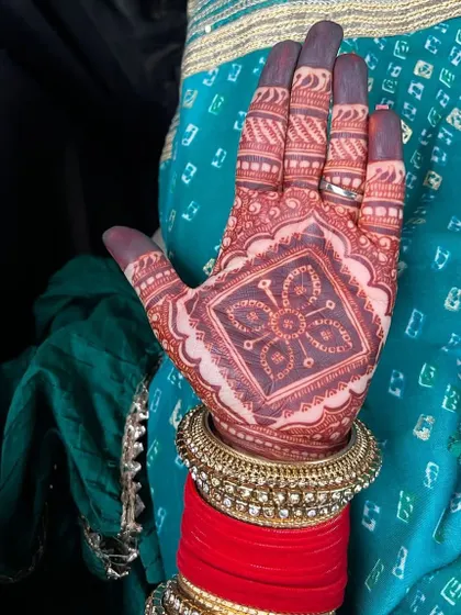The beautiful dark stain on a happy client's hand, perfectly complemented by her traditional red and gold bangles.