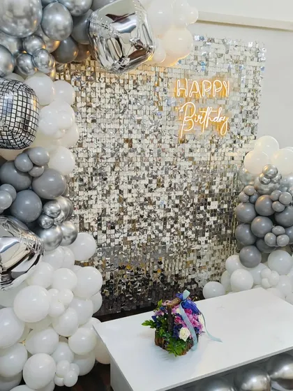A dazzling disco-themed birthday party. We used a silver shimmer wall, a white and grey balloon arch with disco ball foil balloons, and a neon sign to create this fun setup.