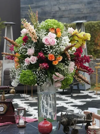 A table adorned with vintage props like an old-fashioned telephone and an hourglass, alongside a large, colorful floral arrangement.