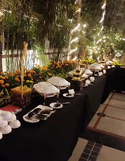 A full view of our garden-themed evening buffet. The black tablecloth provides a beautiful contrast to the white serveware, marigold flower arrangements, and the surrounding illuminated palm trees.