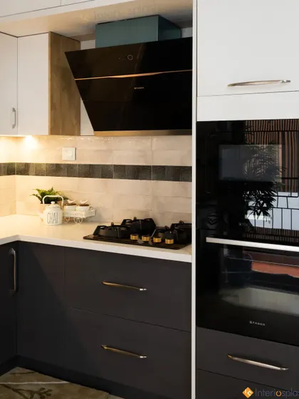 This kitchen features a bold contrast with dark grey lower cabinets and white upper cabinets. The design includes a built-in oven and a sleek black chimney for a modern, high-end look.