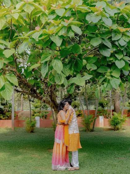 An intimate embrace under a canopy of green leaves. This photo captures the couple's close bond and the romantic atmosphere of their garden celebration.