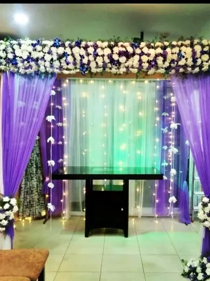 A simple flower decor setup for Ganesh Chaturthi. We used purple drapes, a white and blue floral header, and fairy lights to create a beautiful space for the deity.