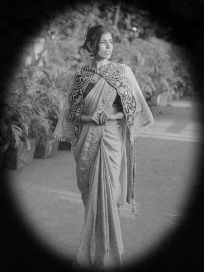 A full-length, vintage-style black and white photo, portraying a timeless and classic look in a draped saree with an embroidered cape.