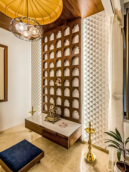 This pooja unit is set against a wall with a beautiful jali pattern featuring multiple niches for idols. The design is both traditional and space-efficient.