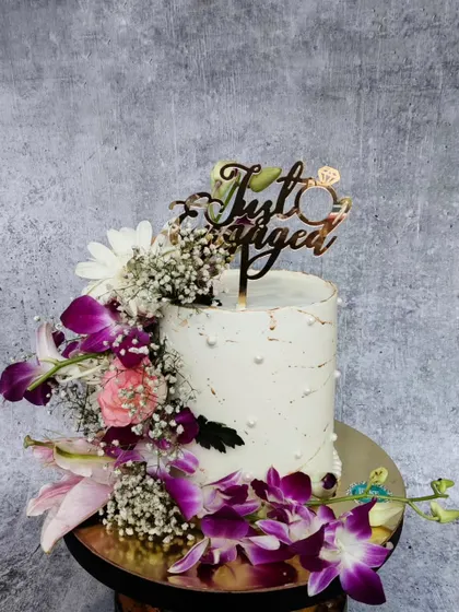 A simple yet stunning engagement cake adorned with a cascade of fresh purple orchids and other delicate flowers. The "Just Engaged" topper adds the perfect finishing touch.