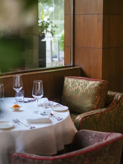 A cozy corner table, set for an intimate meal. The plush, patterned chairs and crisp white tablecloth create a sense of occasion.