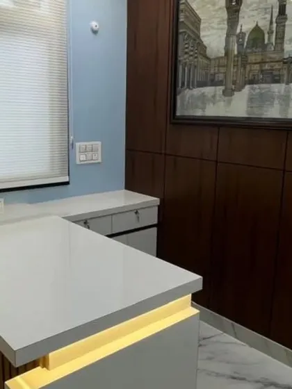 The director's cabin in the Lucknow office. A clean, white L-shaped desk with built-in lighting is paired with a rich wood-paneled wall to create a professional and stylish workspace.