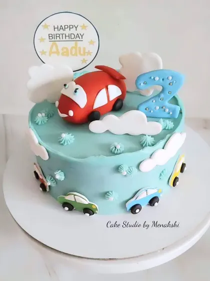 A sweet car themed cake for Aadu's second birthday. The design features a cute red car on top of a blue cake with fluffy clouds.