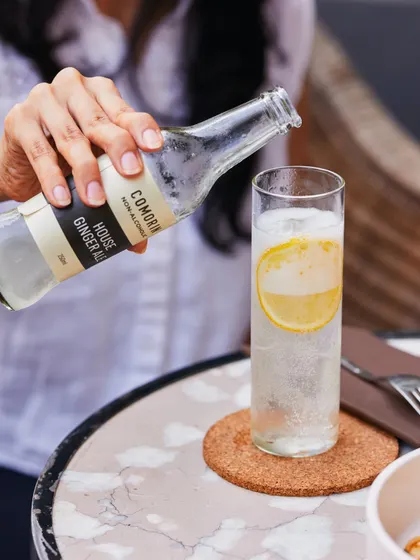 A hand pours our house Ginger Ale over ice, creating a simple, elegant, and refreshing non-alcoholic drink.