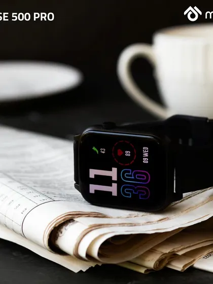 The smartwatch is placed on a folded newspaper next to a coffee cup. This classic morning routine setup gives the modern tech a timeless, relaxed, and sophisticated feel.