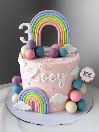 A cheerful cake with rainbows and peaches. This tall pink cake is decorated with pastel rainbows and colorful chocolate balls, perfect for a happy celebration.