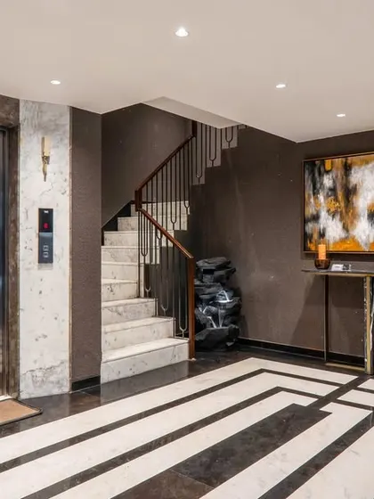 The elegant lift lobby and staircase area, showcasing a blend of rich textures and artistic touches. The design uses dark walls, patterned marble floors, and a statement art piece to create a posh, sophisticated atmosphere.