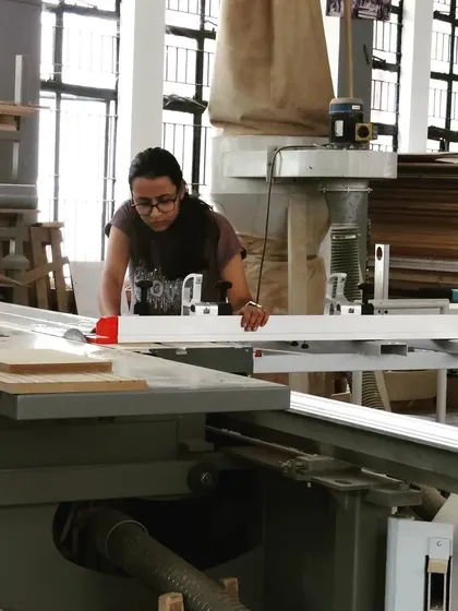 A student operates a large panel saw, a machine essential for accurately cutting down large sheets of plywood and MDF for panel-based furniture.