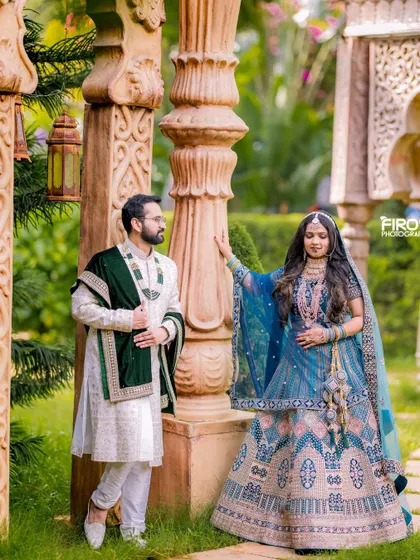 A regal portrait of a couple in stunningly detailed traditional outfits. The lush garden and ornate pillars provide a perfect backdrop for this elegant shot.