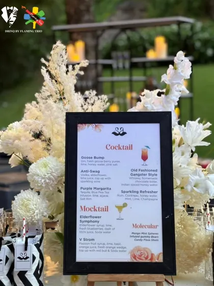 An elegant black and white themed bar setup for an outdoor event. The design features custom glassware tags and is complemented by beautiful white floral arrangements.