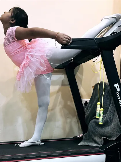 A young ballerina practices a backbend stretch using the treadmill for support.