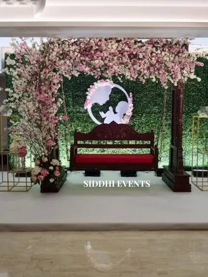 Celebrating new beginnings with this enchanting baby shower decor. A classic wooden swing, adorned with a canopy of delicate pink cherry blossoms against a green hedge wall, creates a beautiful and serene setting for the mother-to-be.