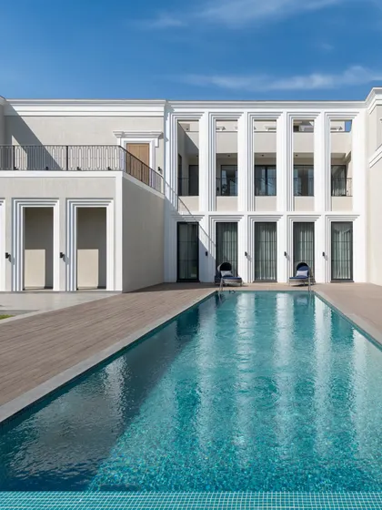 The clean geometry of this modern-classical facade is softened by the tranquil blue of the swimming pool. We design homes as complete experiences, where every exterior view is composed with artistic intent.
