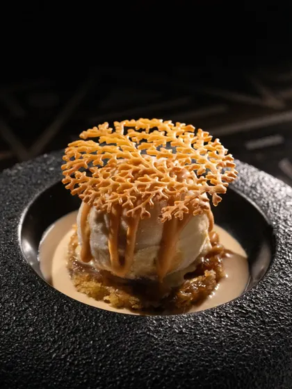 A scoop of vanilla ice cream with a caramel drizzle and a delicate sugar tuile. The dark, moody lighting makes this dessert feel luxurious.
