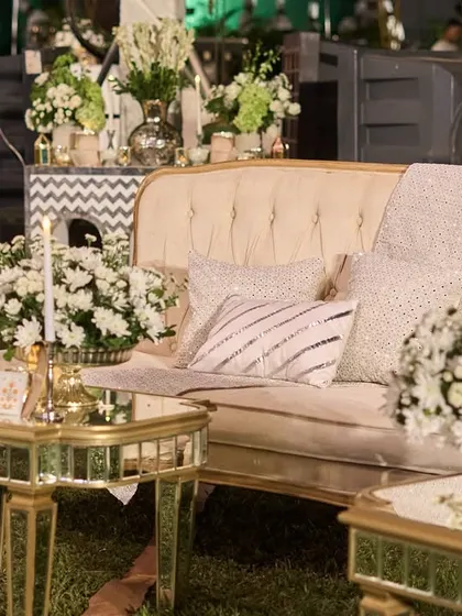 A lounge area with vintage-style cream sofas and mirrored tables. The space is filled with bouquets of white chrysanthemums, creating a serene and royal atmosphere.