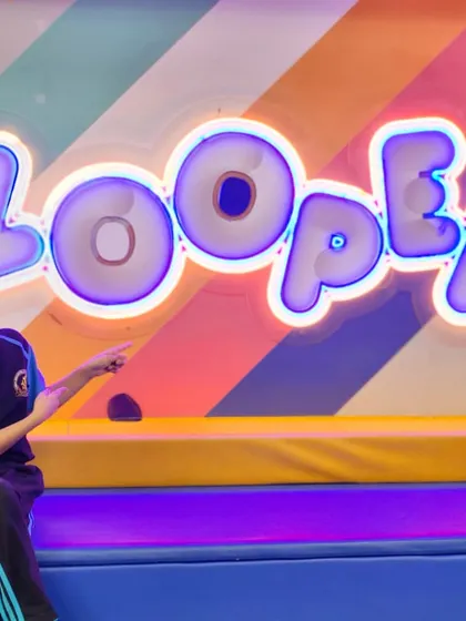 A student points to the glowing Zooper sign, ready for more fun. The colorful decor adds to the exciting atmosphere.