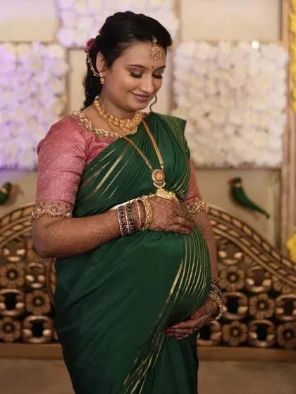 A full-length view of the baby shower look. The makeup and hairstyle are designed to complement the traditional green saree and intricate gold jewelry perfectly.