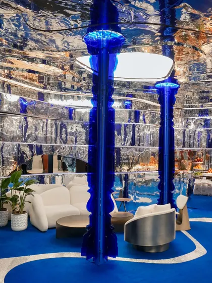 Two glowing cobalt columns anchor the space, their traditional form reimagined in a futuristic material. They act as sculptural elements that draw the eye and bathe the installation in a vibrant blue light, enhancing the immersive quality of the design.
