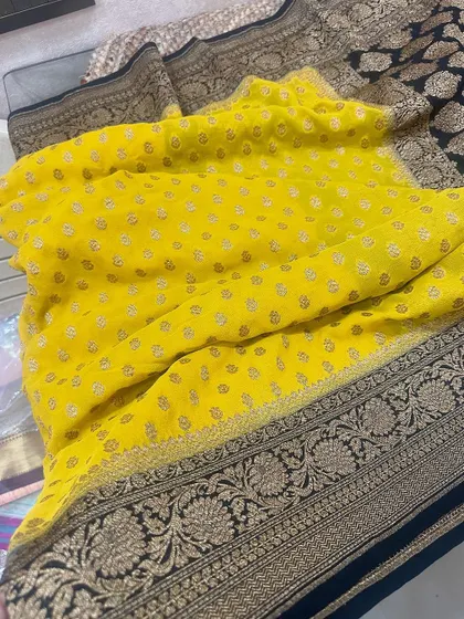 A close-up of the yellow Kadi georgette saree with its black border, showing the beautiful texture and gold buti work.