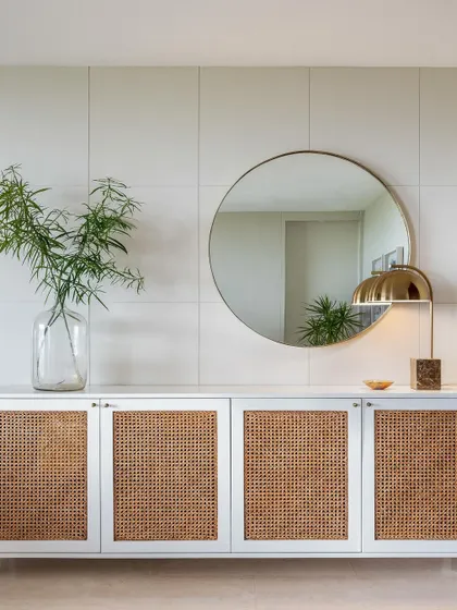 This custom credenza features cane-front doors and sits against a wall of large-format tiles. The round mirror and brass lamp complete this clean, modern, and textural moment.