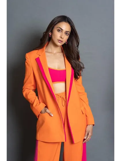 A full-length shot of the vibrant orange and pink pantsuit from Antithesis. The wide-leg trousers and oversized blazer create a modern and powerful silhouette.