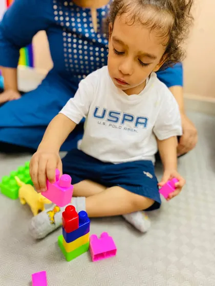 A toddler concentrates on stacking colorful blocks, an essential play activity for developing spatial awareness, fine motor skills, and an early understanding of physics.