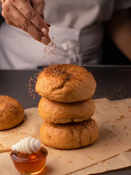 The art of baking in a single shot. Here, we capture a chef sprinkling brown sugar on a stack of fresh bagels, with a pot of honey nearby, creating a warm and artisanal feel.