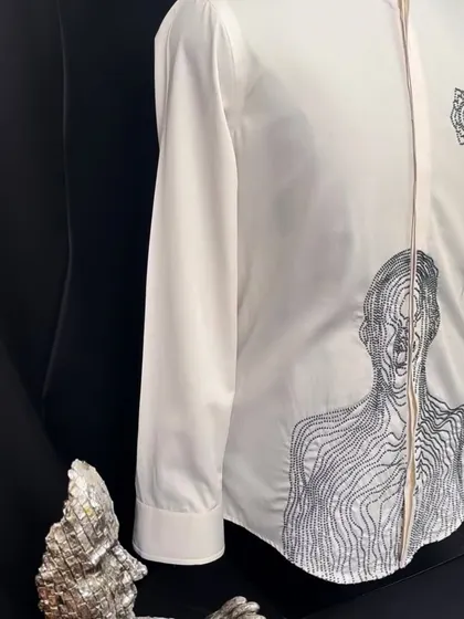 Another angle of the abstract-figurative white shirt, displayed with metallic art pieces that echo its modern, sculptural feel.