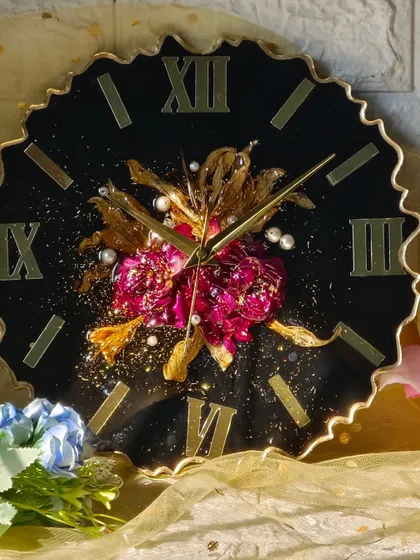 For a touch of drama, this clock features a black face with a central cluster of preserved pink and gold flowers. The gold Roman numerals and hands complete the luxurious look.