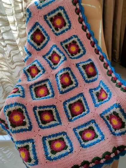 The Lydia blanket draped over a chair, showing how the soft pink fabric and colorful squares can brighten up a room.