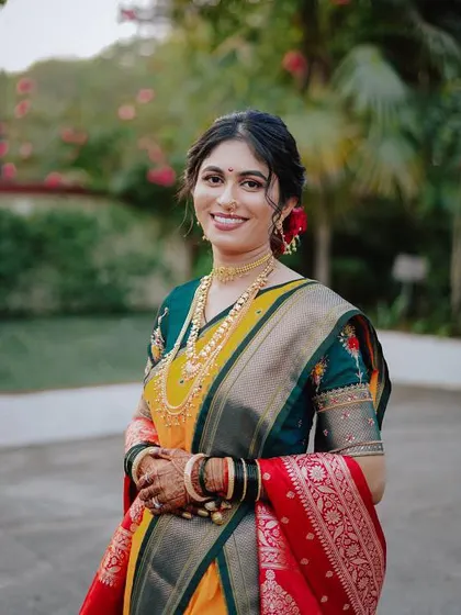 A happy bride in her Nauvari saree. The makeup is fresh and radiant, with a simple hair updo adorned with flowers, perfect for a traditional Maharashtrian wedding.