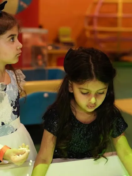 Two girls concentrate on an activity at one of our interactive play tables.