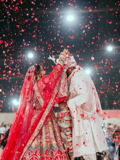 A classic varmala shot, with the couple exchanging garlands under a shower of red rose petals, a timeless and romantic image.
