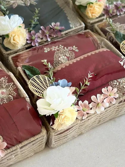 We use natural jute-wrapped baskets to give trousseau gifts a rustic yet elegant feel. These baskets are decorated with delicate floral arrangements, perfectly complementing the traditional wedding outfits inside.