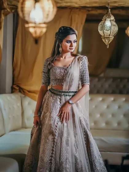 A stunning solo portrait of the bride in her intricately embroidered lehenga. The warm lighting and her elegant pose create a timeless and regal image.