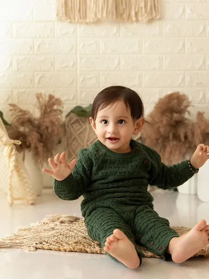 A pre-cake smash portrait from a boho session, with the baby sitting on a jute mat in a cozy green outfit.