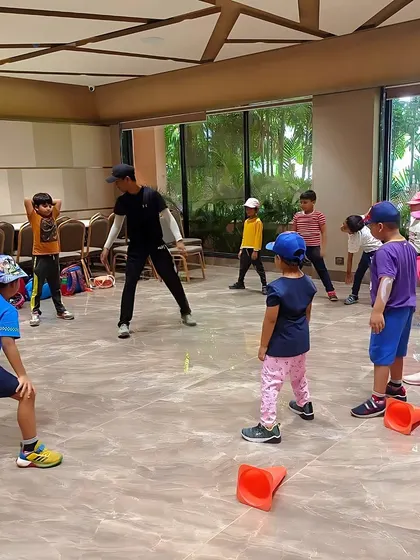A coach leads a group of children in a warm-up exercise. Our sessions always start with proper preparation to ensure the kids are ready for physical activity.
