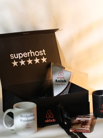 An angled view of the Airbnb "Superhost" gift box, showing the personalized trophy, branded mug, and other curated items nestled inside. The presentation is designed to feel exclusive and celebratory.