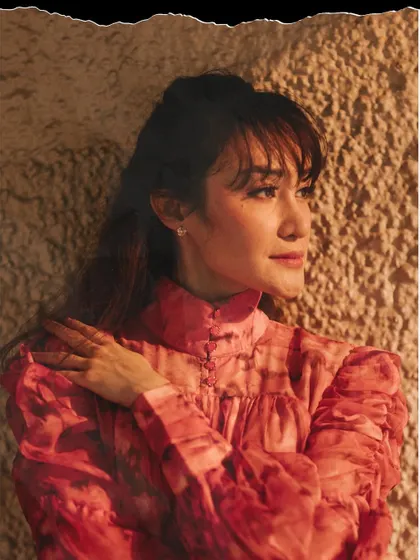 A close-up portrait using warm, dramatic lighting. The play of light and shadow on the textured wall adds depth and a painterly quality to the image.
